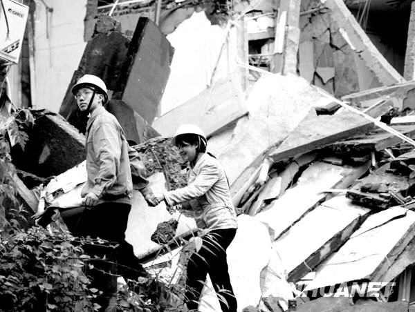 2008年5月13日，东方汽轮机厂领导将一位向废墟里喊话的女青年（右）从十分危险的废墟旁带走。东方汽轮机厂是四川德阳一大型国有企业，地震发生后，有近千名员工、家属遇难或失踪。这位女青年的弟弟所在的科研车间中有多名科研人员被掩埋，眼看着亲人被埋在废墟中无法施救，勇敢的姐姐走近十分危险的废墟，哭喊着鼓励弟弟坚强地活下来。